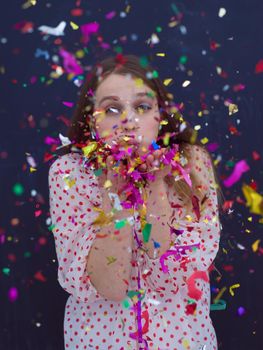beautiful young woman celebrating new year and chrismas party while blowing confetti decorations to camera isolated over gray background