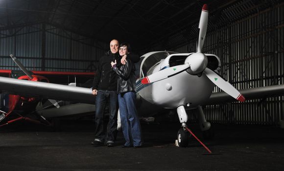 beautiful and happy young couple  posing in front of an old retro private propeler airplane and representing happines wealt and rich life concept