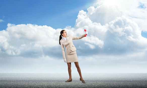 Young woman looks scared at retro phone in her hand. Fearful secretary in white business suit with phone standing on road outdoor. Hotline support service. Business assistance and consultation concept