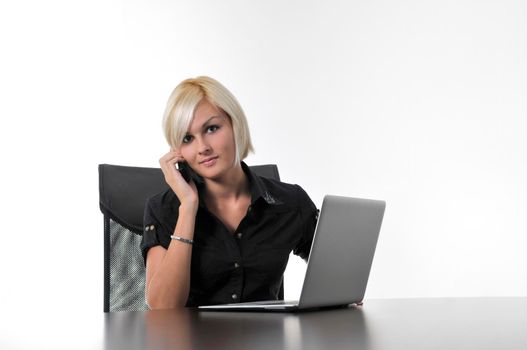 One young business blonde woman working in office on laptop and talking on cellphone, isolated image