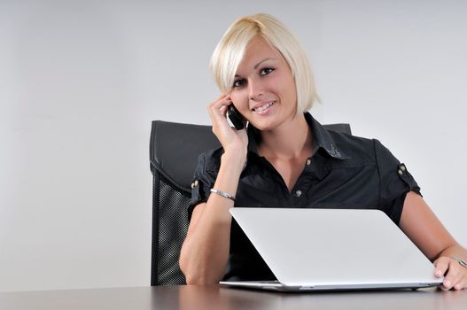 One young business blonde woman working in office on laptop and talking on cellphone, isolated image
