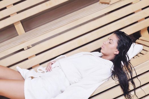 Pretty Young woman take a steam bath treatment at finish wooden sauna while wearing white towel