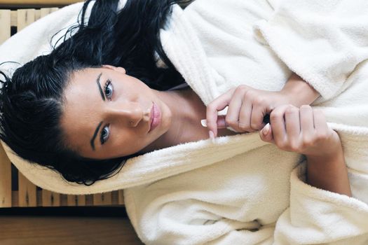 Pretty Young woman take a steam bath treatment at finish wooden sauna while wearing white towel