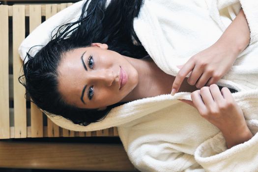 Pretty Young woman take a steam bath treatment at finish wooden sauna while wearing white towel