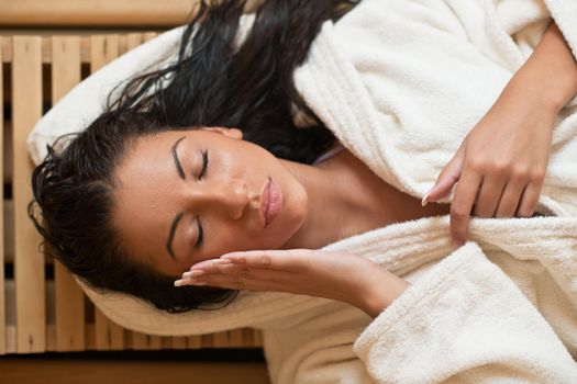 Pretty Young woman take a steam bath treatment at finish wooden sauna while wearing white towel