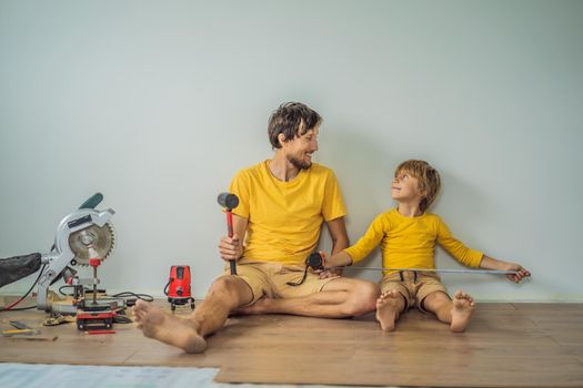 Father and son installing new wooden laminate flooring on a warm film floor. Infrared floor heating system under laminate floor.