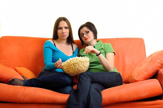 female friends eating popcorn and watching tv at home on orange sofa isolated on white