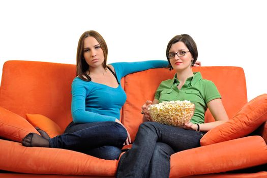 female friends eating popcorn and watching tv at home on orange sofa isolated on white