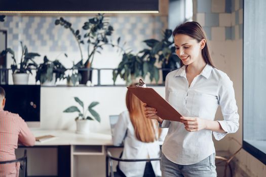 Portrait of a young attractive businesswoman holding clipboard in modern office
