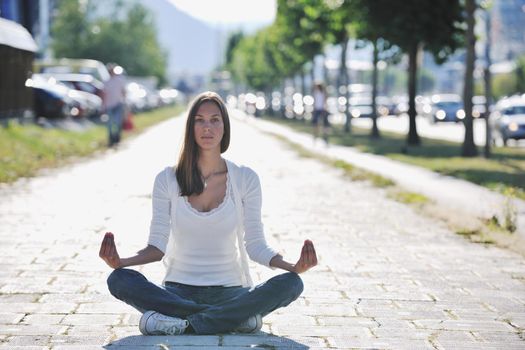 beautiful young woman meditating and exercise yoga in lotus position at street at beautiful sunny day with blured background