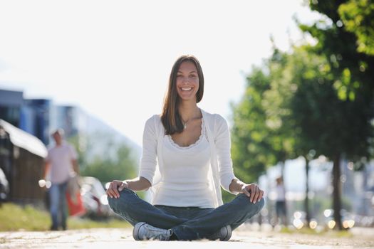 beautiful young woman meditating and exercise yoga in lotus position at street at beautiful sunny day with blured background