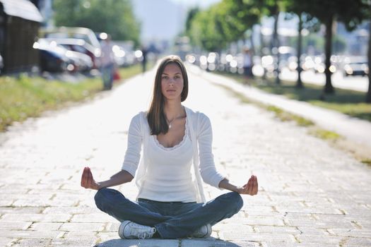 beautiful young woman meditating and exercise yoga in lotus position at street at beautiful sunny day with blured background