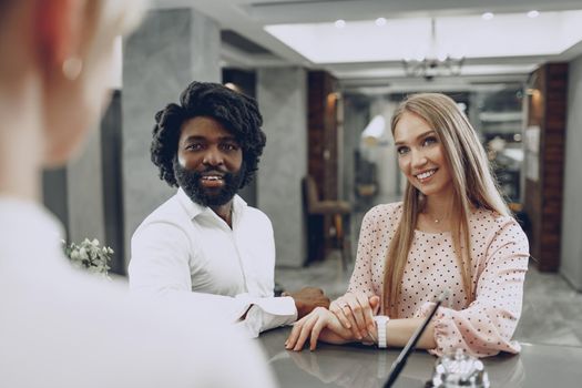 Business trip concept. Black man and caucasian woman businesspeople colleagues checking-in in hotel reception desk