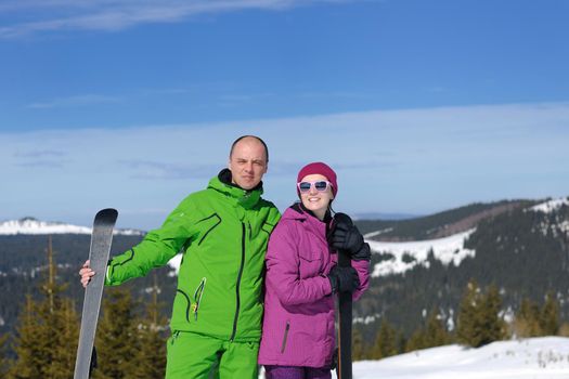 Portrait of happy couple at beautiful mountain on winter sunny day with blue sky and snow in background