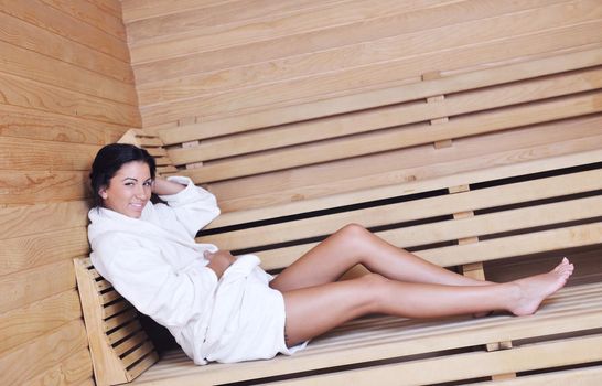 Pretty Young woman take a steam bath treatment at finish wooden sauna while wearing white towel