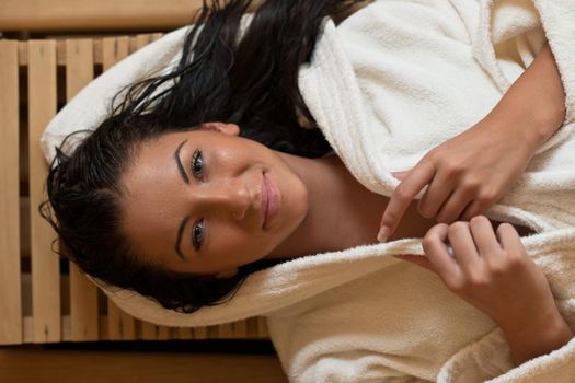 Pretty Young woman take a steam bath treatment at finish wooden sauna while wearing white towel