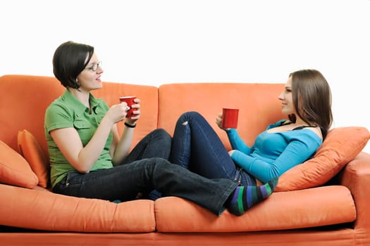 two young woman isolated on white with cup off coffee talking and chating isolated on whtie on orange sofa