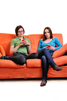 two young woman isolated on white with cup off coffee talking and chating isolated on whtie on orange sofa