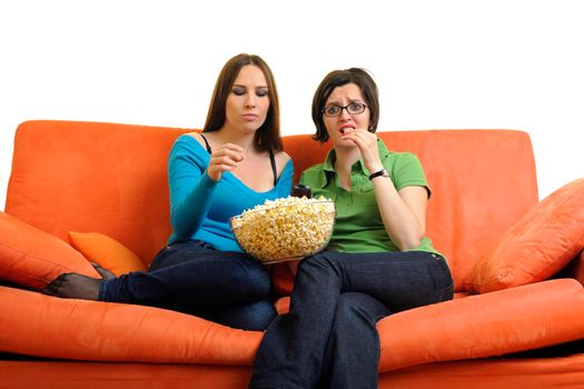 female friends eating popcorn and watching tv at home on orange sofa isolated on white