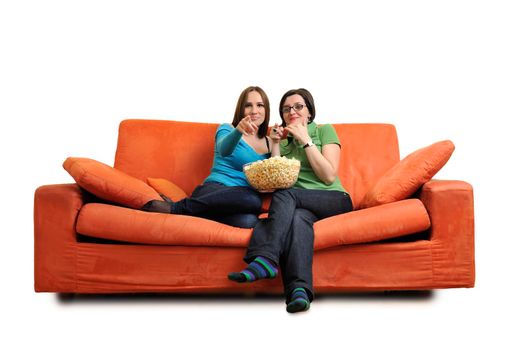 female friends eating popcorn and watching tv at home on orange sofa isolated on white