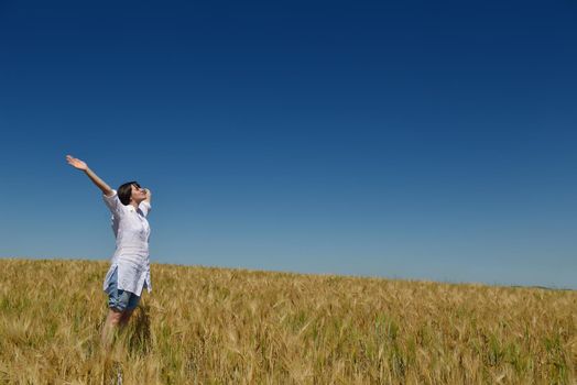 Young woman standing jumping and running  on a wheat field with blue sky in  background at summer day representing healthy life and agriculture concept