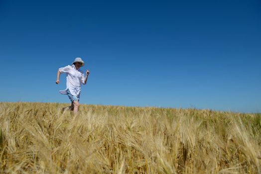 Young woman standing jumping and running  on a wheat field with blue sky in  background at summer day representing healthy life and agriculture concept
