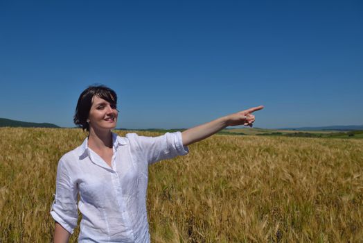 Young woman standing jumping and running  on a wheat field with blue sky in  background at summer day representing healthy life and agriculture concept