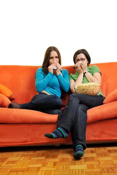 female friends eating popcorn and watching tv at home on orange sofa isolated on white