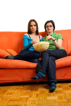 female friends eating popcorn and watching tv at home on orange sofa isolated on white