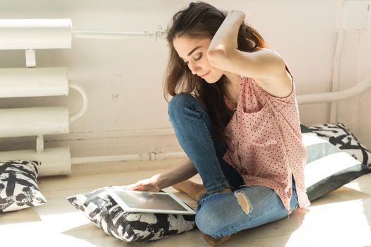 Technologies, people concept - young woman sitting on sofa and watching the tablet or surfing the net and smiling.