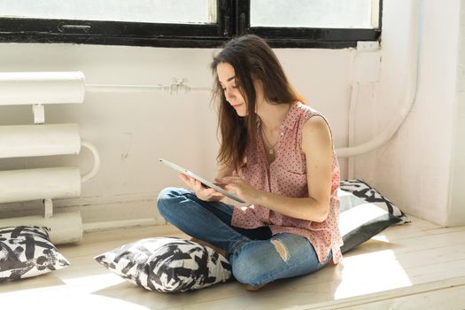 Technologies, people concept - young woman sitting on sofa and watching the tablet or surfing the net and smiling.