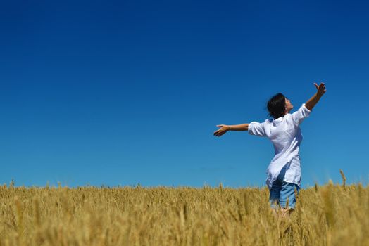 Young woman standing jumping and running  on a wheat field with blue sky in  background at summer day representing healthy life and agriculture concept