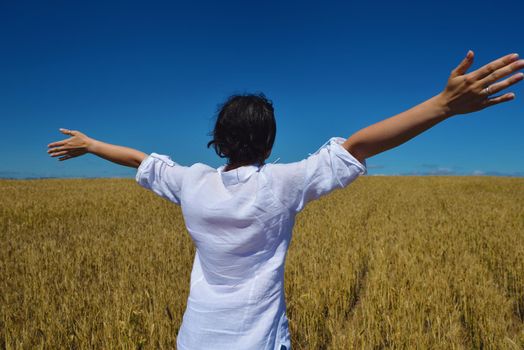 Young woman standing jumping and running  on a wheat field with blue sky in  background at summer day representing healthy life and agriculture concept