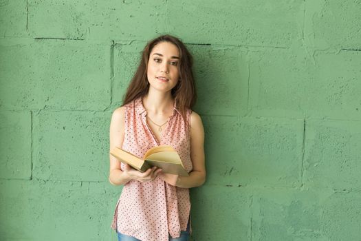 Literature, education, people concept - Female student in reading the book over the green wall.