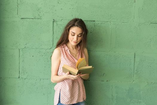 Literature, education, people concept - Female student in reading the book over the green wall.