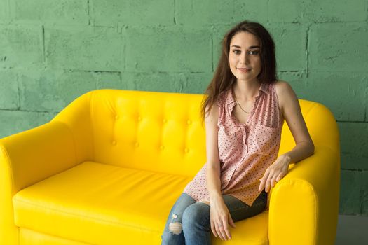 Young student woman is sitting on the yellow sofa.
