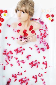 woman beauty spa and wellness treathment with red flower petals in bath with milk 