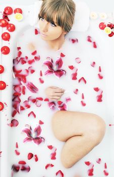 woman beauty spa and wellness treathment with red flower petals in bath with milk 