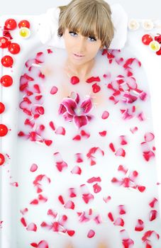 woman beauty spa and wellness treathment with red flower petals in bath with milk 