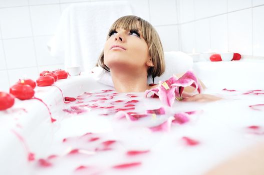 woman beauty spa and wellness treathment with red flower petals in bath with milk 