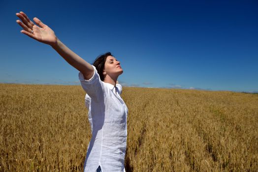 Young woman standing jumping and running  on a wheat field with blue sky the background at summer day representing healthy life and agriculture concept