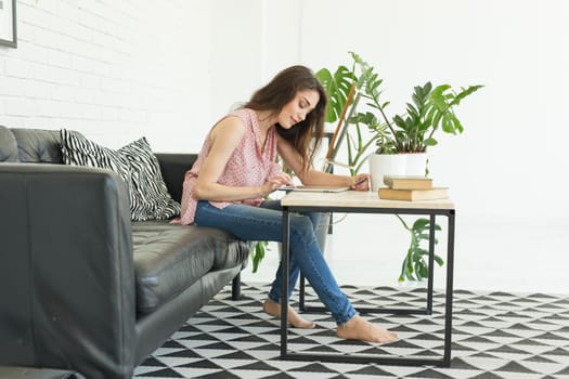 people, education and interior concept - young woman sitting nesr a table and using a tablet.