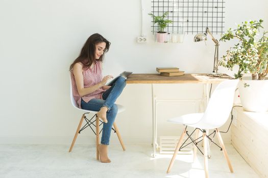 Technologies, communication, people concept - young woman is sitting on sofa and chatting in tablet and smiling.