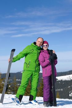 Portrait of happy couple at beautiful mountain on winter sunny day with blue sky and snow in background