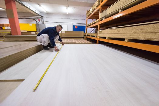 young man carpenter measuring wooden board for cutting while working in big modern carpentry High quality wood concept