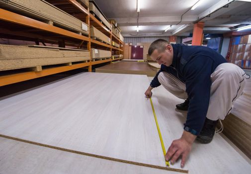 young man carpenter measuring wooden board for cutting while working in big modern carpentry High quality wood concept