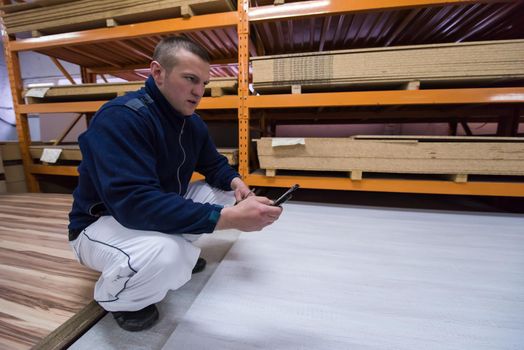 young man carpenter using a mobile phone to calculate measures for wooden board while working in big modern carpentry High quality wood concept