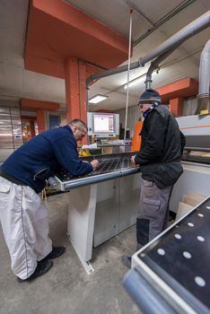 two young carpenters calculating and programming a cnc wood working machine in workshop. wood workers preparing a computer program for CNC machine at big modern carpentry