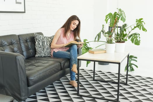 Education and people concept - young woman sitting on the sofa with book.