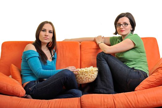 female friends eating popcorn and watching tv at home on orange sofa isolated on white